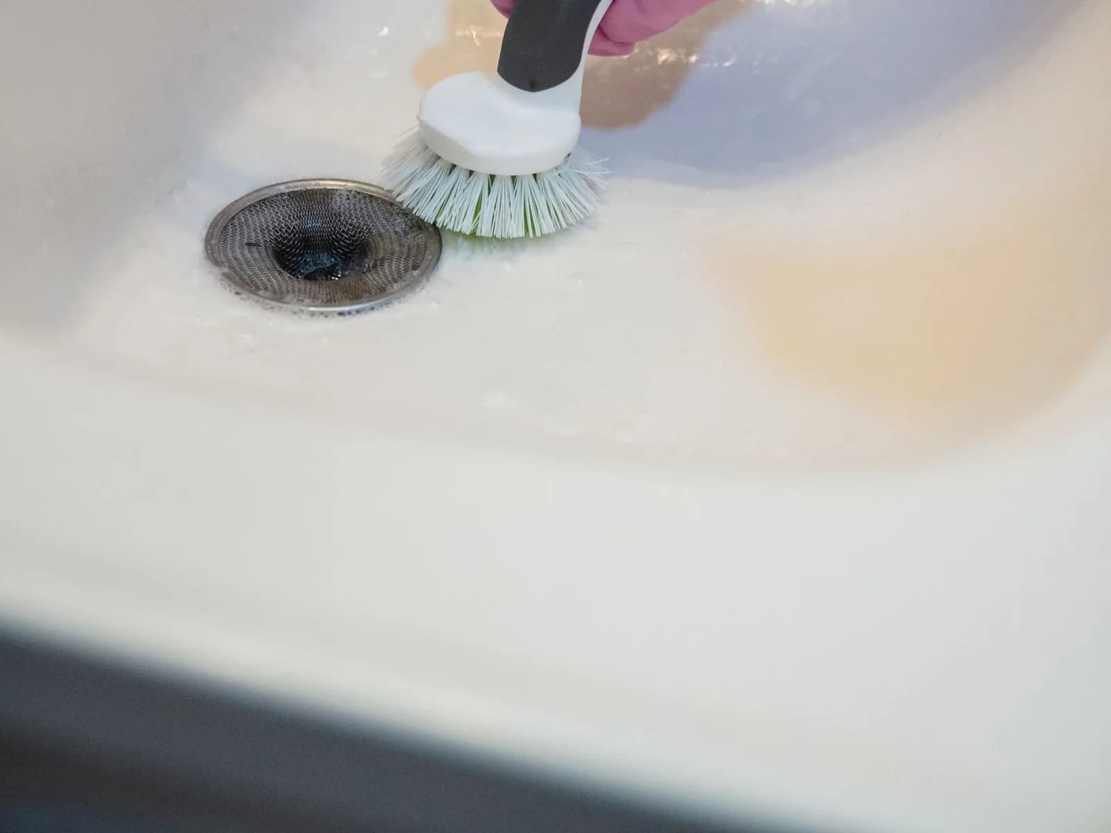 Professional gloved hand deep-cleaning a kitchen sink with a detail brush.